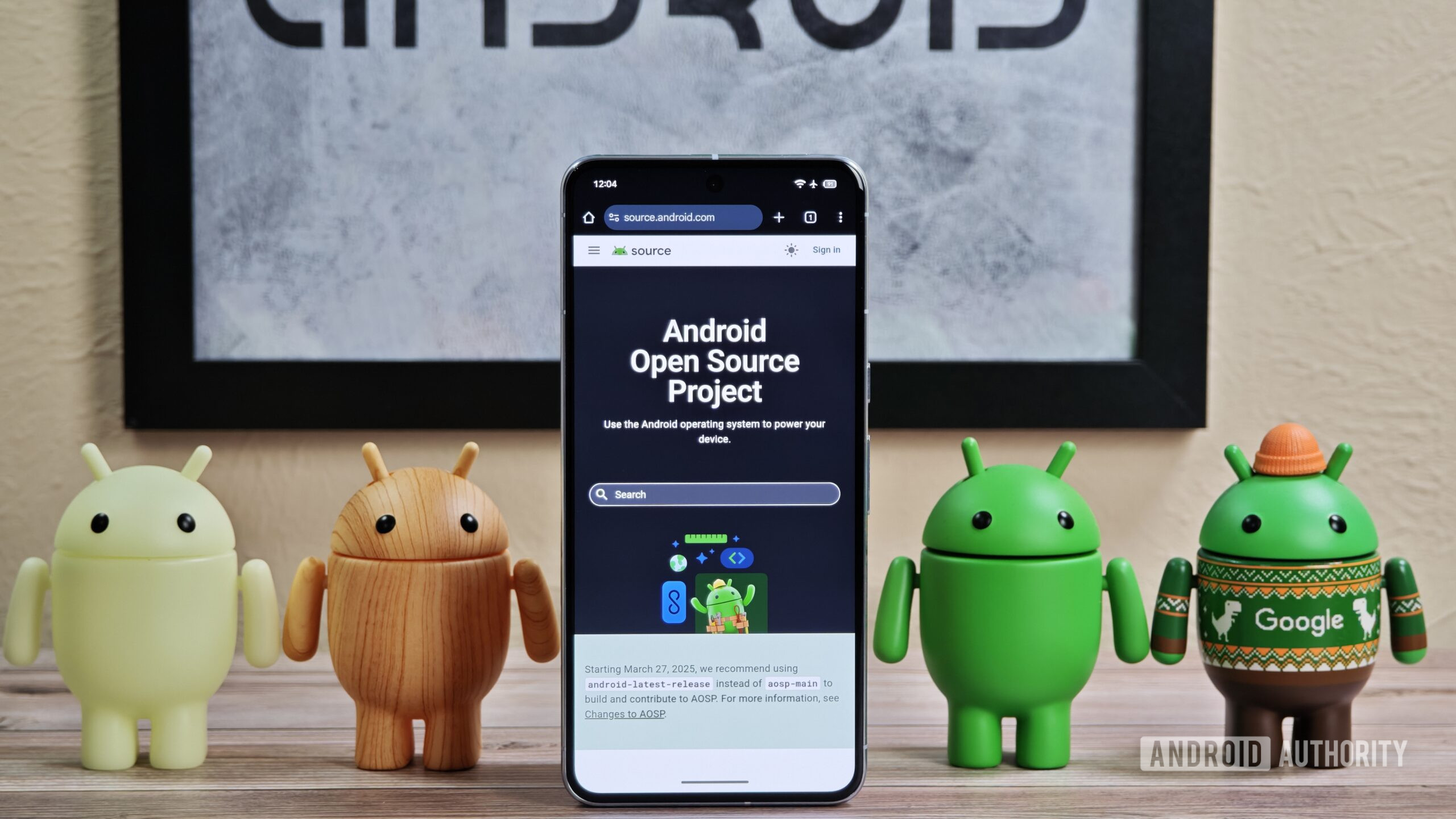 Android figures standing around Pixel phone with AOSP home page showing