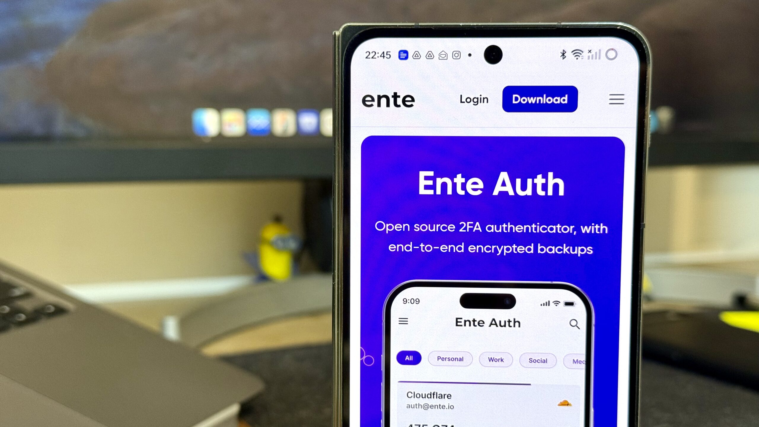 Ente Auth on a phone with a monitor and laptop in the background
