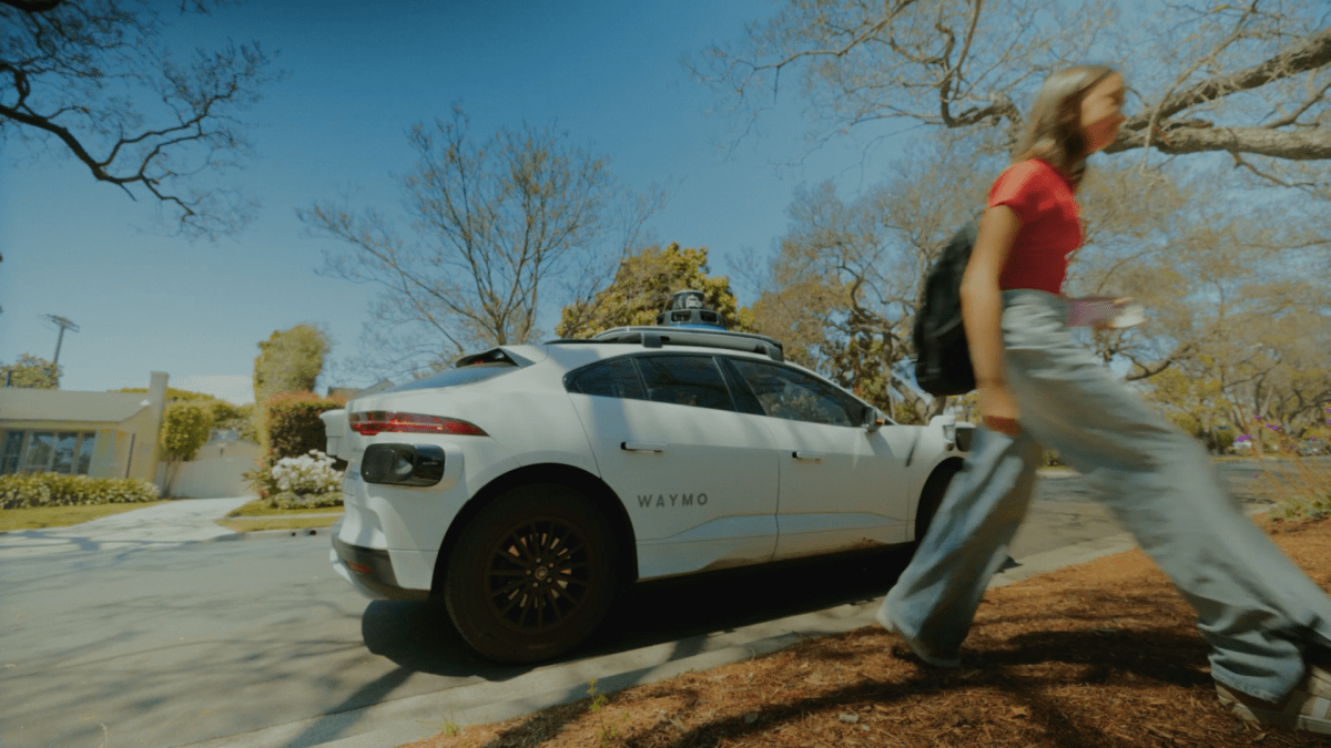 A Waymo robotaxi on the street in Phoenix and a teenage girl walking away from it.