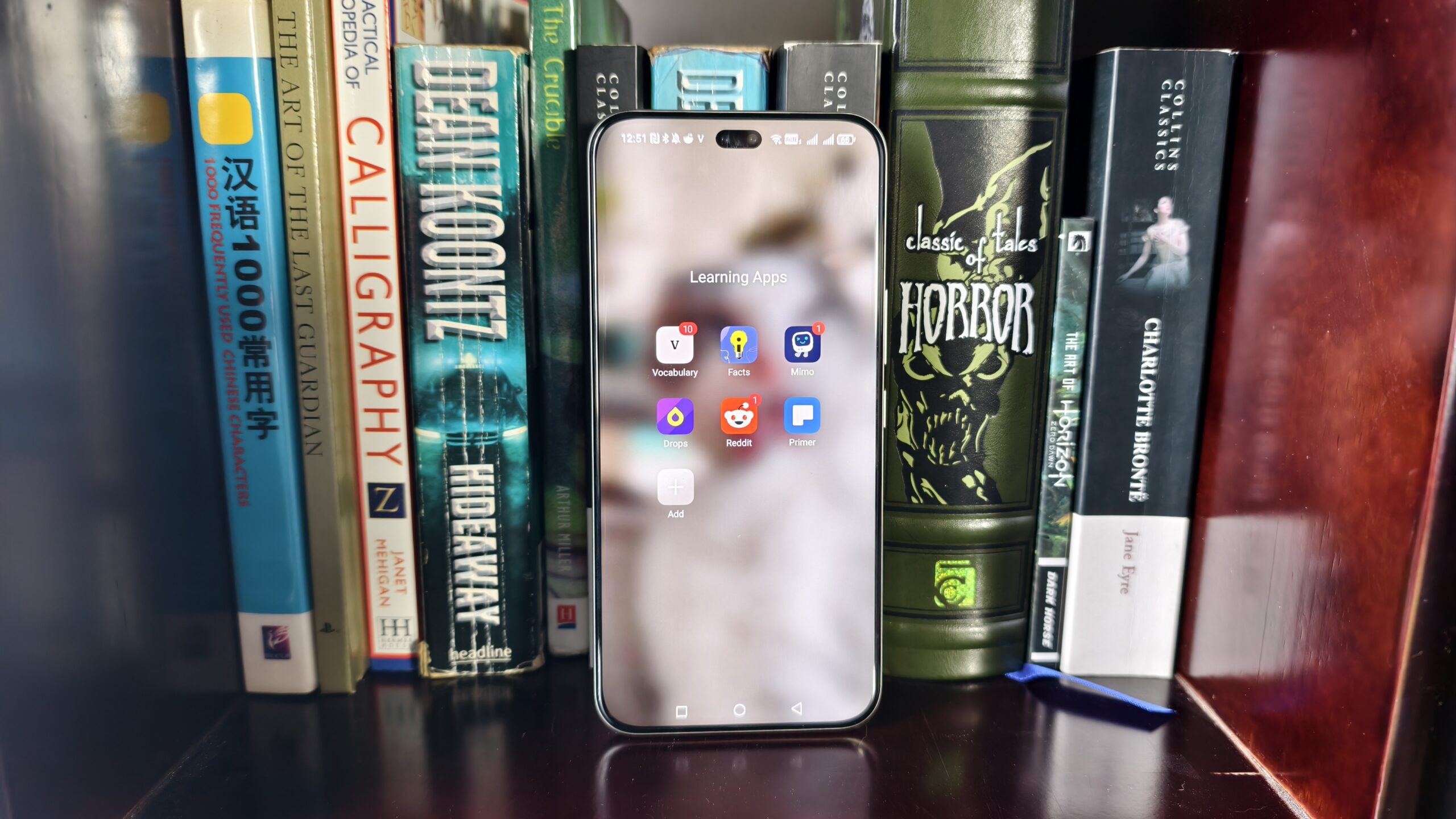 a learning apps folder on a smartphone in front of a range of books